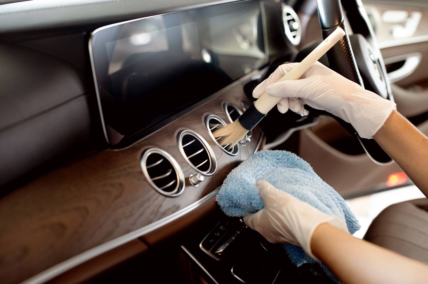 Dashboard vents of a luxury vehicle being detailed with a soft brush and microfiber towel