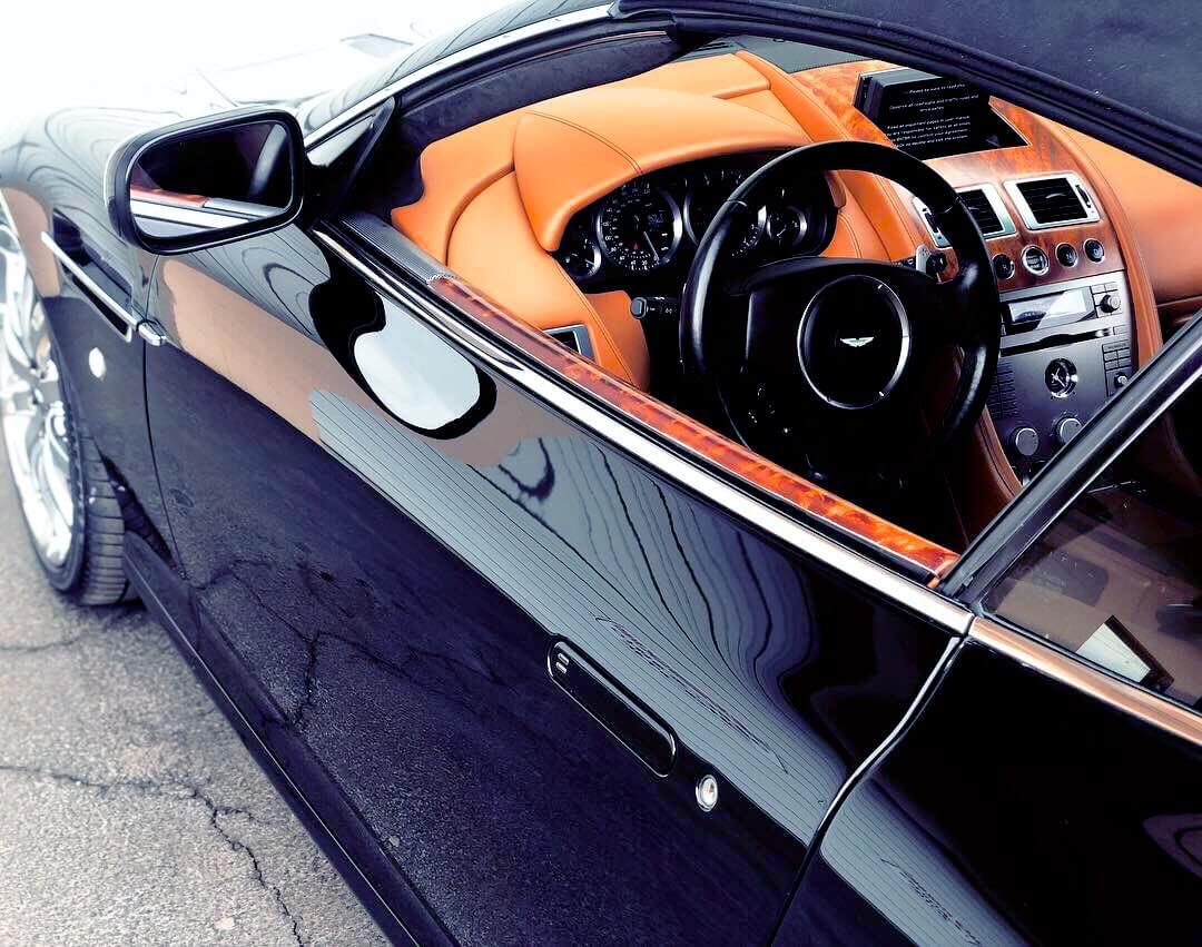 Angled top left peek into the brilliant and sharply clean orange leather interior of a shiny black sedan