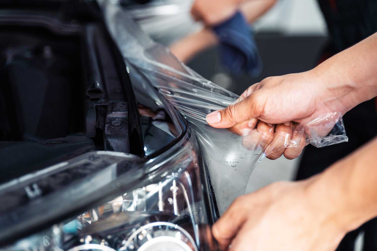 An automotive technician removing chipped paint protection film from black vehicle panel