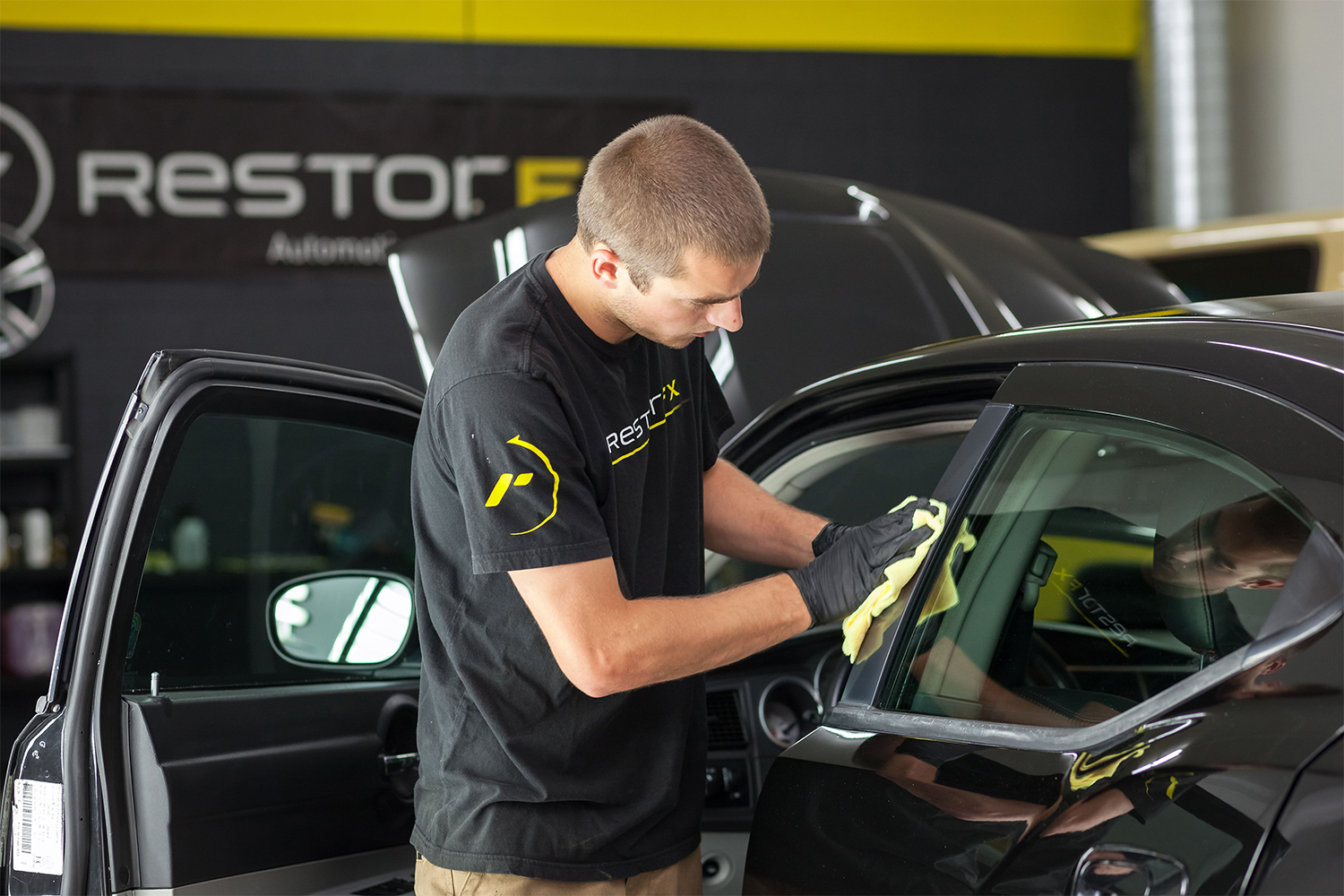 Un técnico de <span  class='notranslate'>RestorFX</span> limpiando la moldura de plástico de la puerta de un automóvil como parte de su restauración